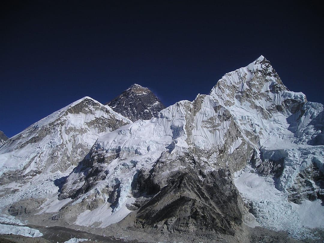 "Panoramic view of Everest Base Camp with colorful tents on the Khumbu Glacier, surrounded by towering Himalayan peaks under a clear blue sky.